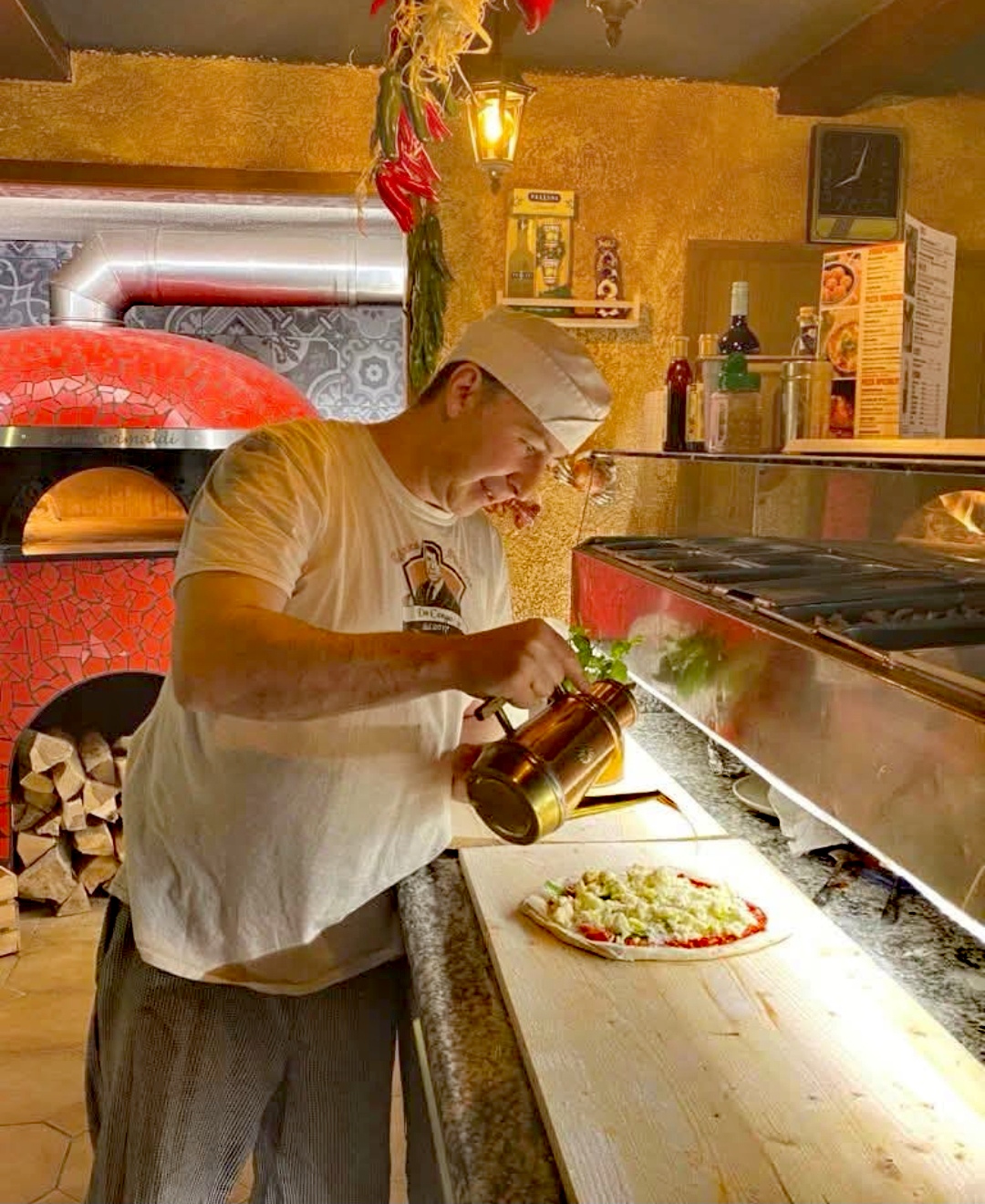 Pizzaiolo belegt eine Pizza direkt am roten Holzofen