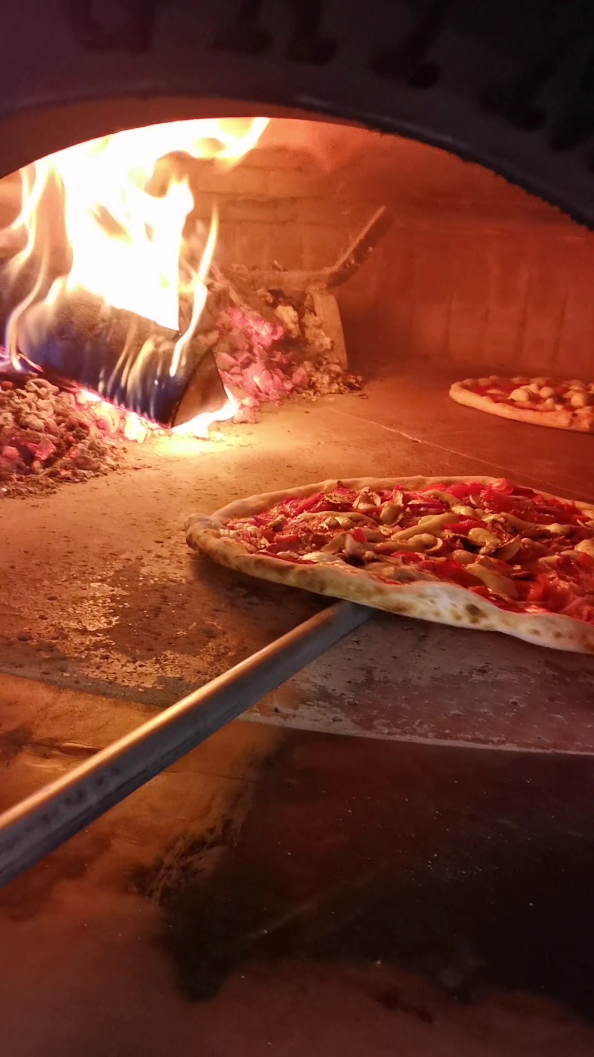 Pizza wird mit der Holzschaufel in den brennenden Ofen geschoben