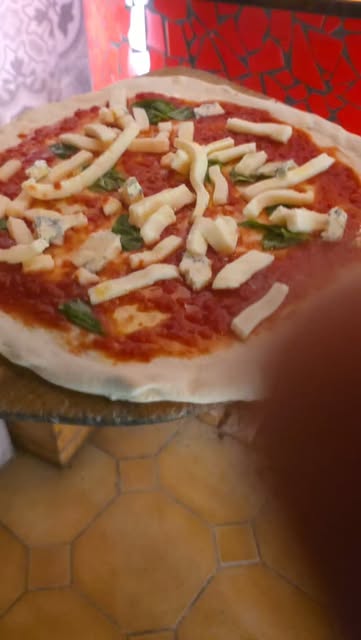 Pizza mit Käsestreifen vor dem roten Mosaik-Ofen